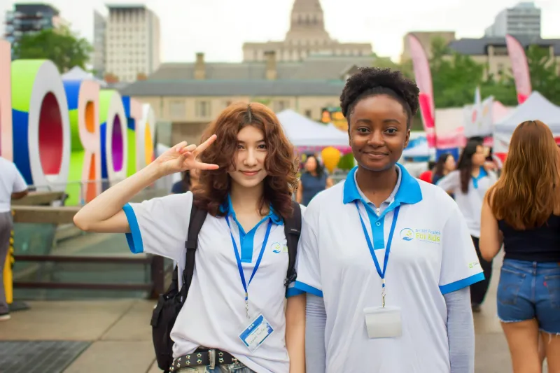 Two smiling volunteers with lanyards at an outdoor event