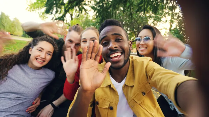 Friends waving hello together in a sunny park
